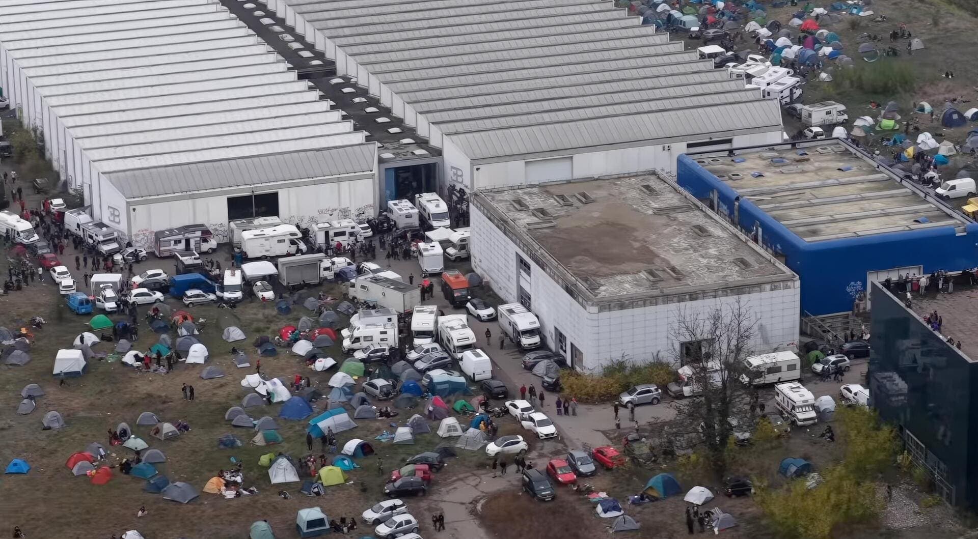 Drone view of the abandoned Bugatti Automobili factory in Campogalliano, Italy, filled with tents, ravers, and vehicles during an unauthorized Halloween rave in 2025.